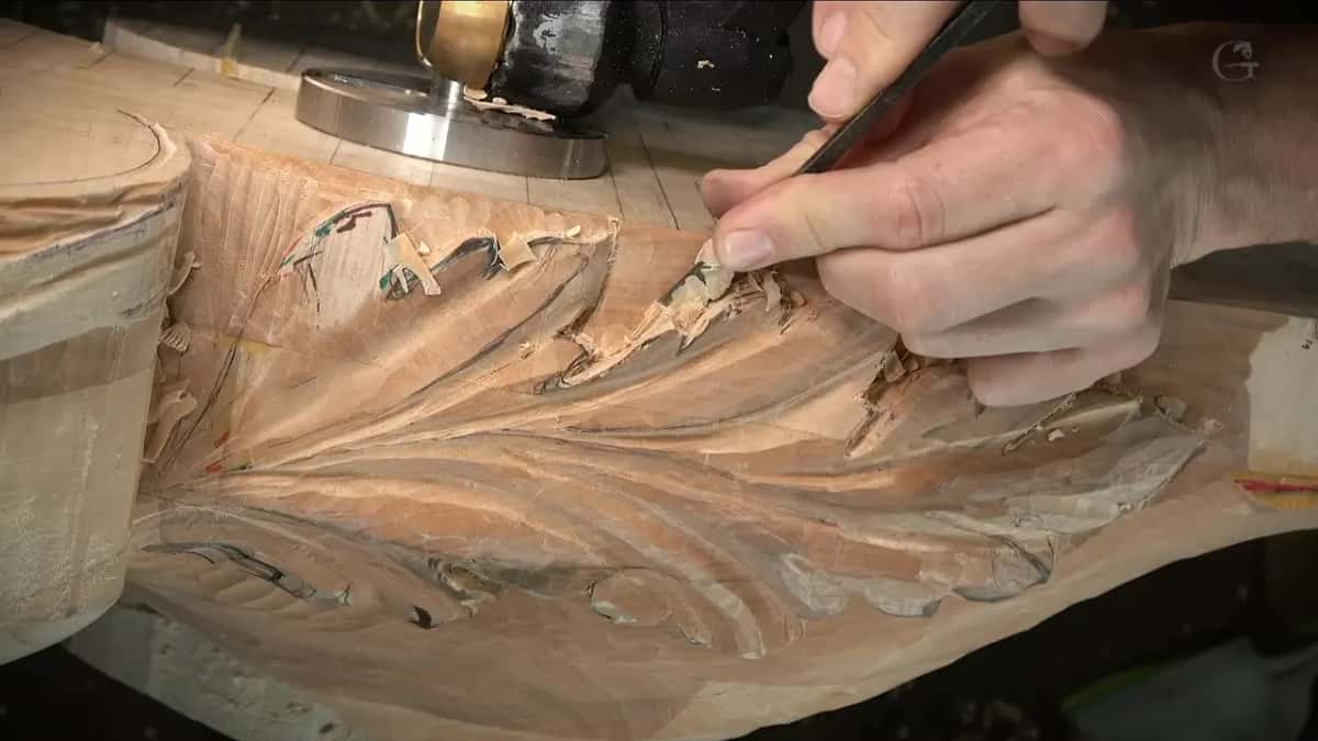 Two fingers pinch a small tool at a lobe tip, a shaving already loose
