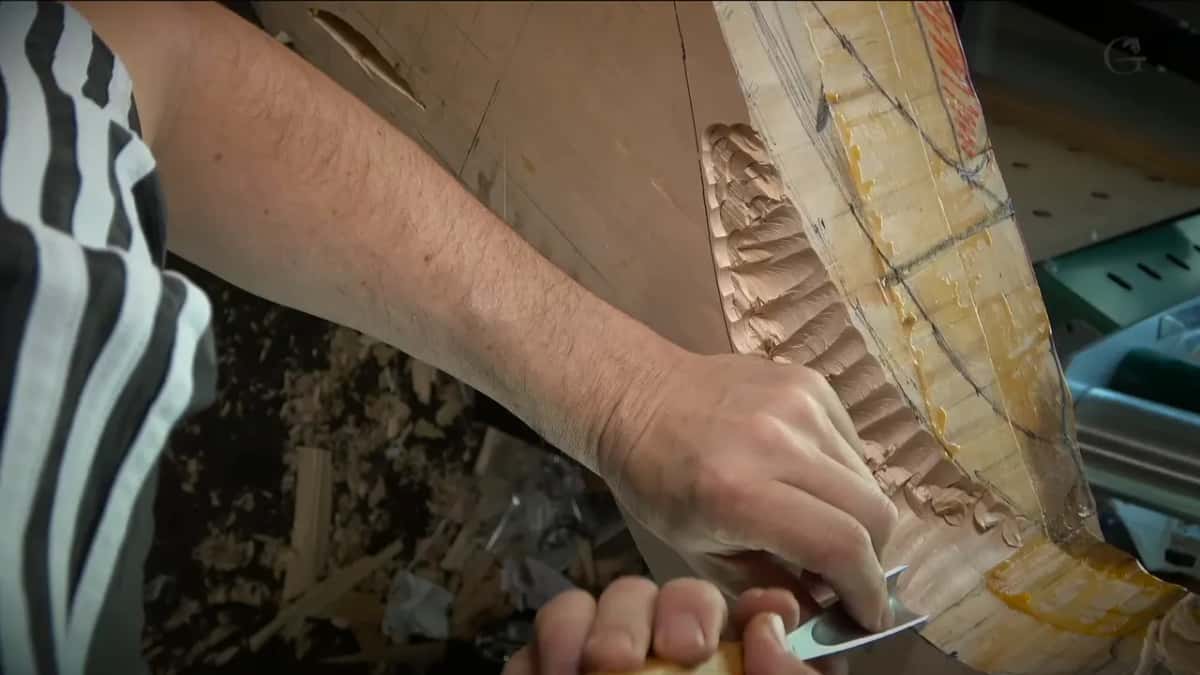 A gouge held low against a wall of scalloped chop marks, a striped sleeve at the edge of the picture
