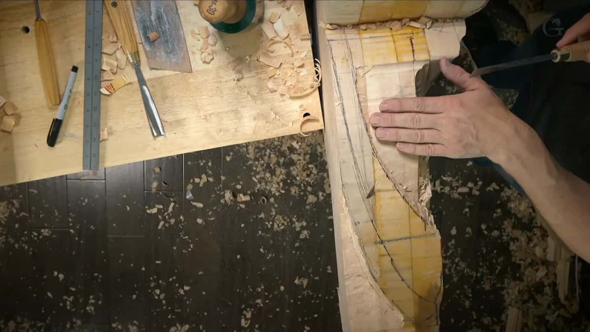 One flat hand rests on the face while the other holds a gouge at its top edge