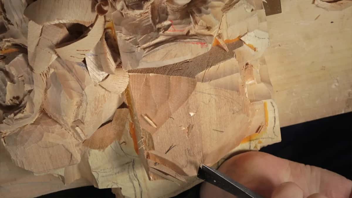Curled chips heaped over the wood and its orange pencil lines
