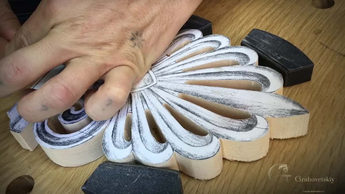 Fingers spread flat on the paper pattern while two black pads grip the sawn blank