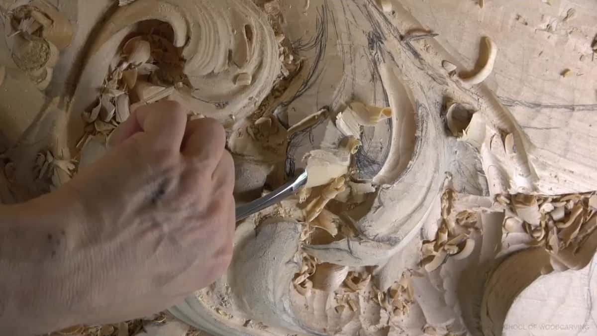 A bent gouge lifts one curl of wood out of the hollow, the shaving standing up off the edge.