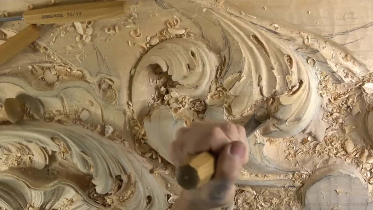 A fist drives a gouge into the acanthus