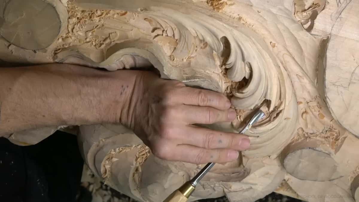 Brass ferrule gouge pressing a concave beside a raised ridge, left fingers guiding it.
