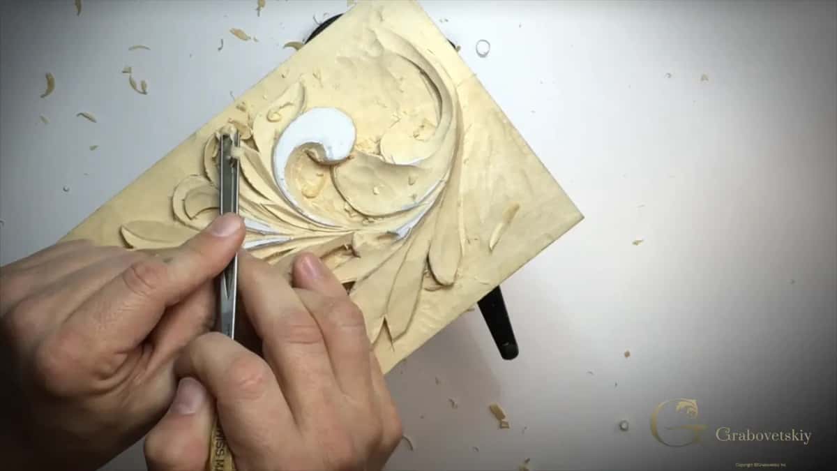 Lifted tool at a lobe left of the top curl, both hands on it, panel tilted