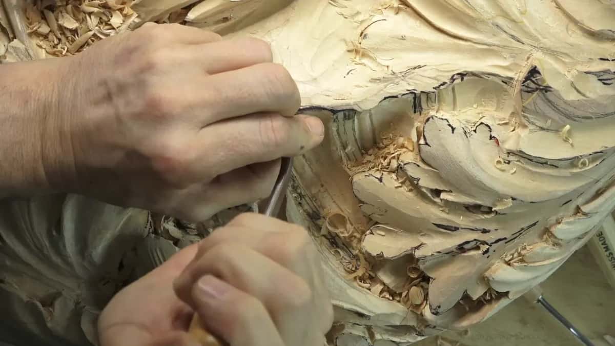 Two hands at work near the top right of the rim, with carved leaves filling the lower half.