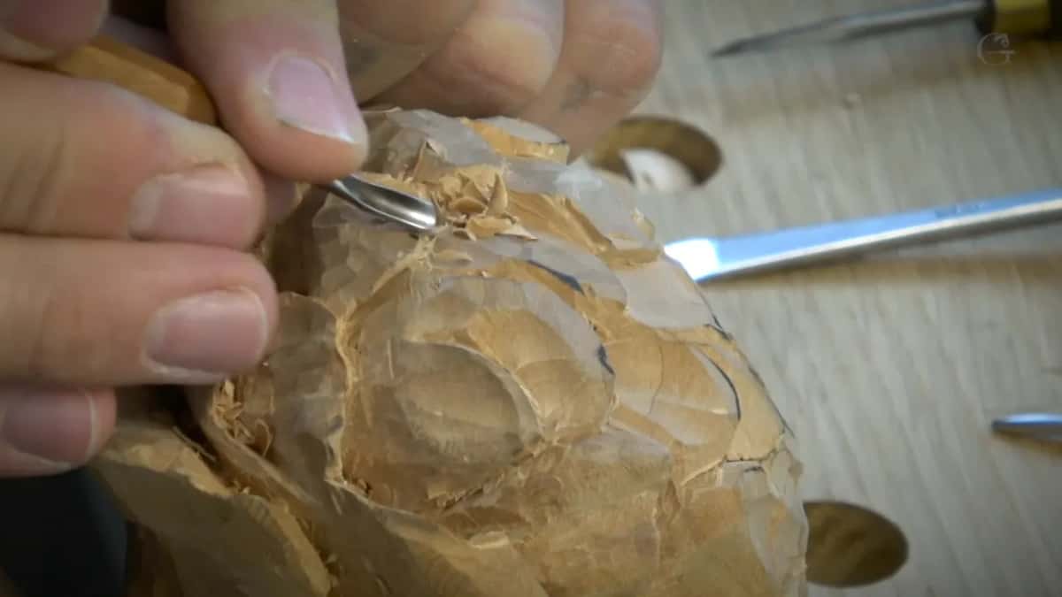 Short curved tool at the top of the flower, other tools and bench holes behind.