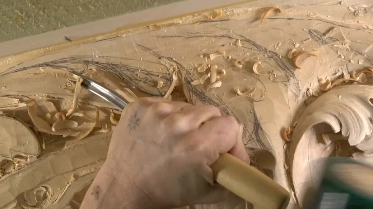 The green mallet sits at the right edge while one hand steers a gouge through the roughed area.