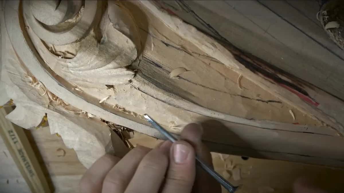 Fingers guide a narrow tool along the lower wall line, a ruler just visible below
