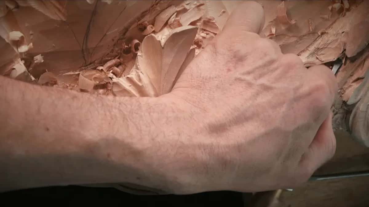 Forearm braced, fist wrapped round the handle, tool pressing into the wood