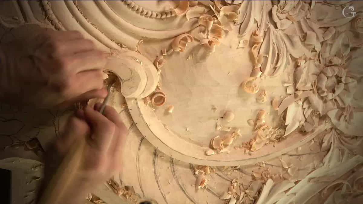 Seen from above, his hands carve inside the scroll while chips pile up on the flat ground