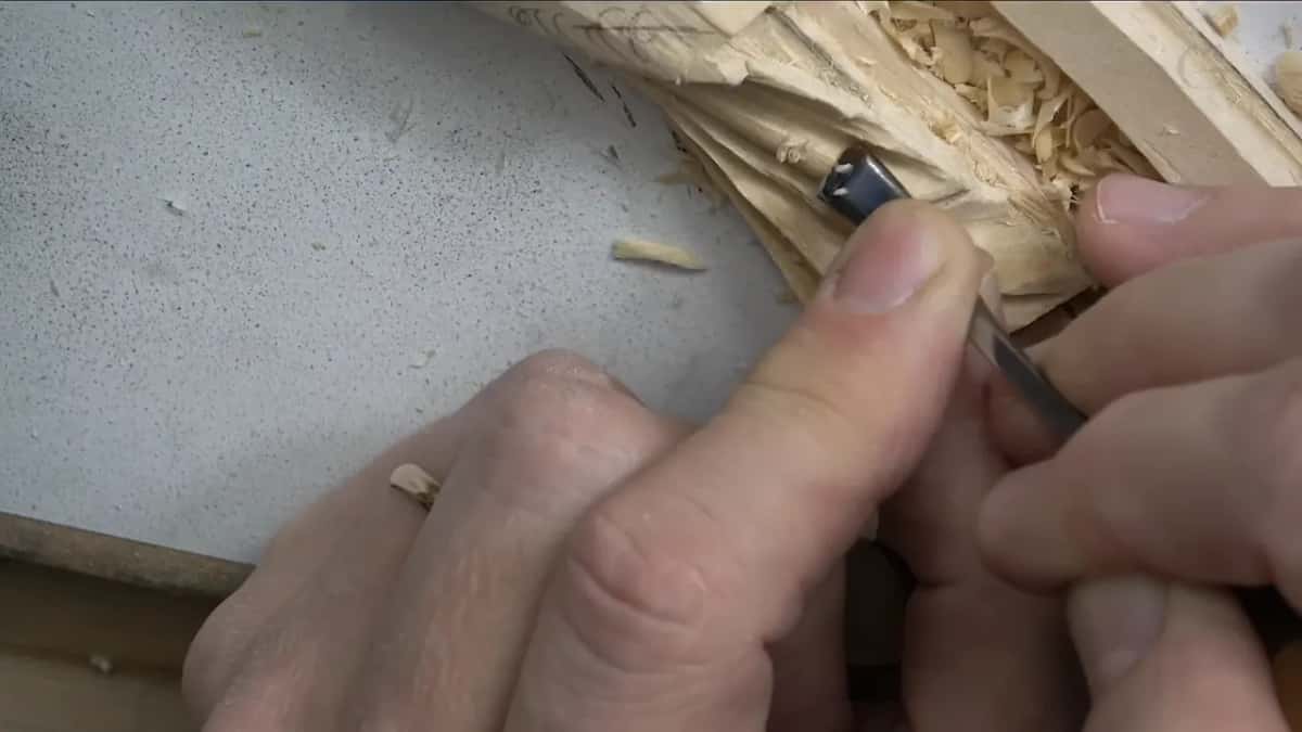 Two hands around one small tool, its tip down in the carved leaf above the white board.