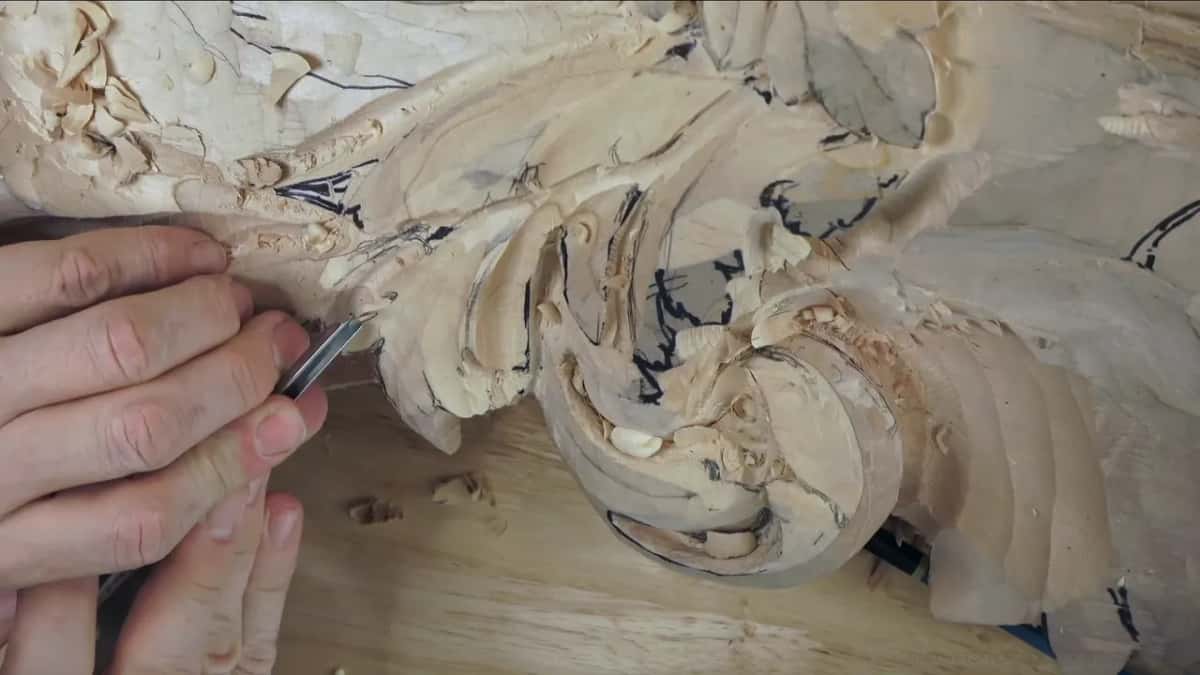 Both hands press a small tool along the edge of a lobe, the leaf's outline still marked in black.