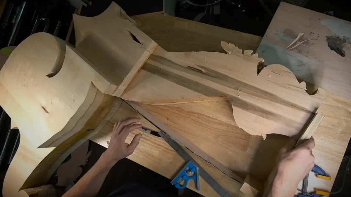 Both hands hold a steel square flat across the side while two blue clamps wait nearby