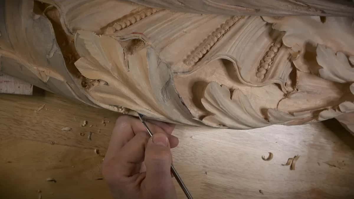 Held low, a thin steel tool runs along the leaf's bottom rim, shavings dotted across the bench