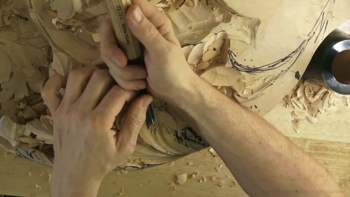 Both hands steering one gouge through drawn scrollwork