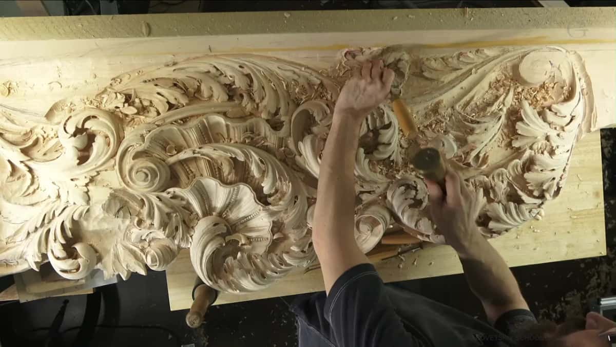 Mallet in one hand, gouge in the other, up in the right corner of the panel