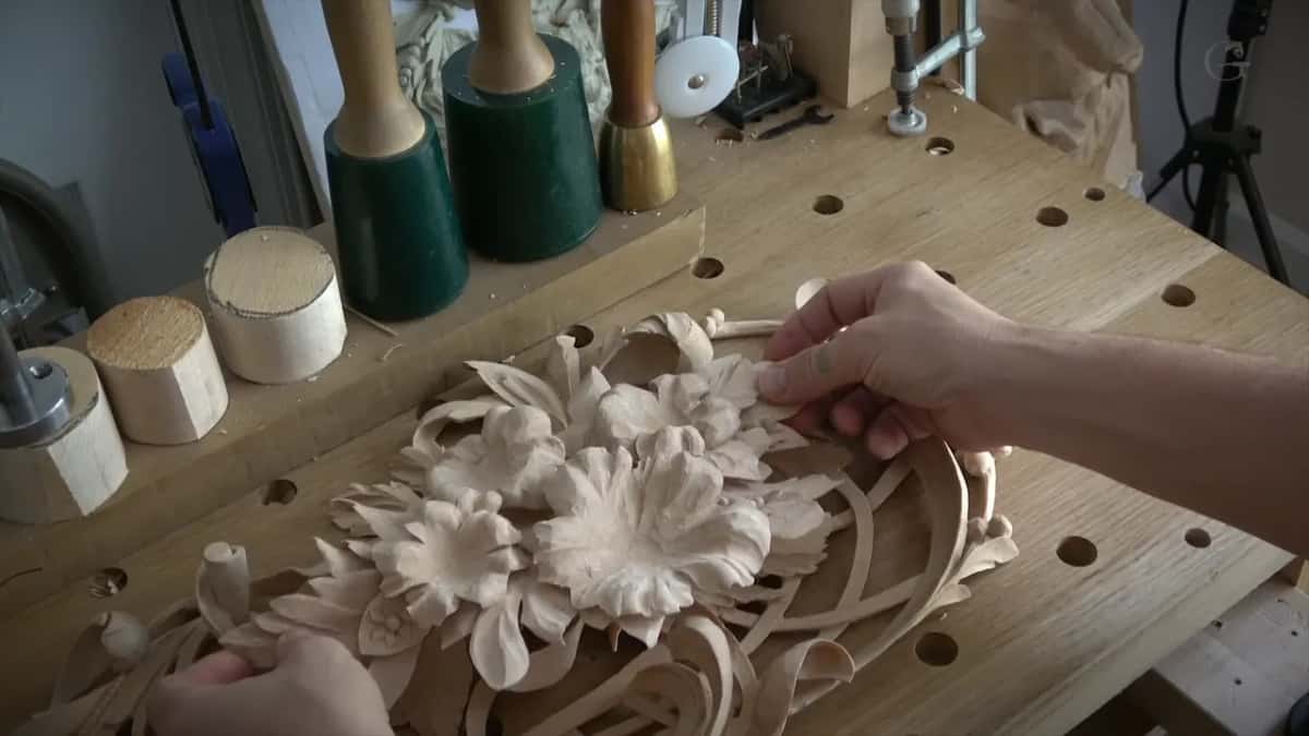 Hands turning the assembled panel with its carved flowers, mallets standing at the back of the bench