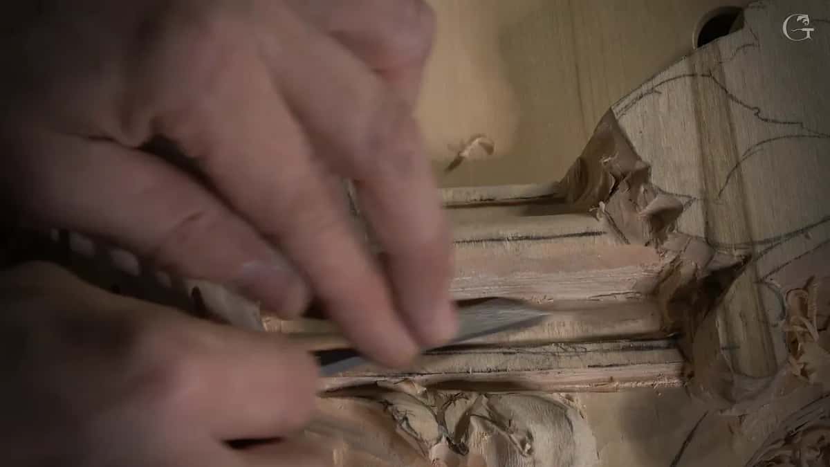 Fingers press a thin flat tool lengthwise along the molding, shavings at the right