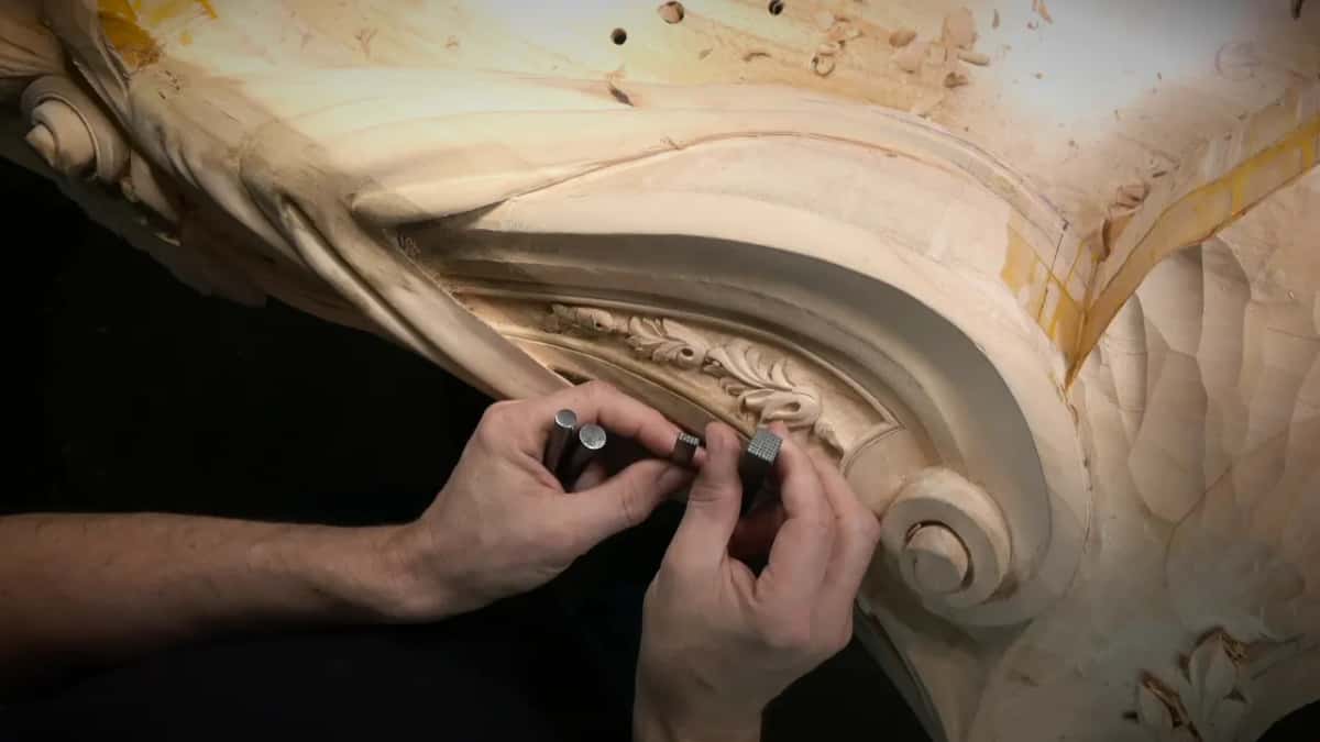 Several punches held up beside a large carved scroll, chips scattered on top